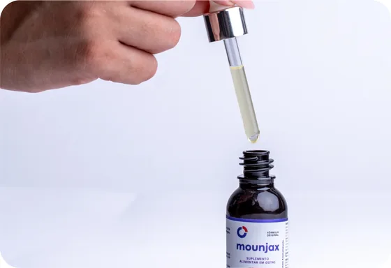 M&atilde;o segurando o conta-gotas de Mounjax sobre o frasco aberto.